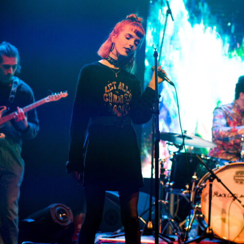 Three band members performing on a well lit stage.