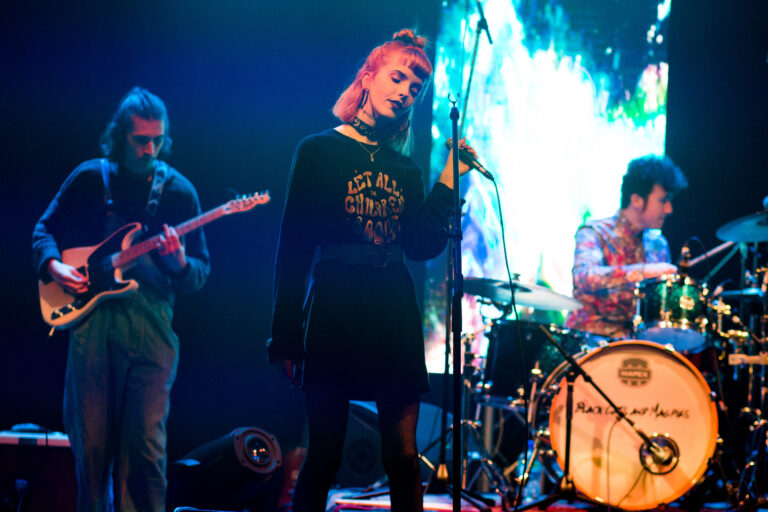 Three band members performing on a well lit stage.
