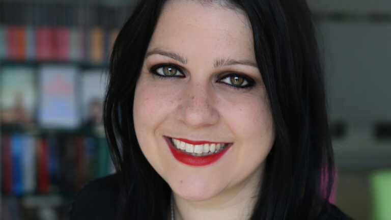 A headshot of Janina Ramirez wearing dark clothing and smiling at the camera.