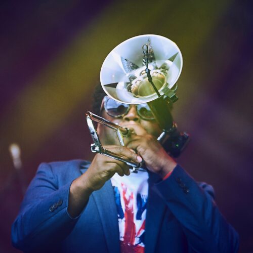 Dennis Rollins wearing a blue blazer and white shirt, playing a trumpet.
