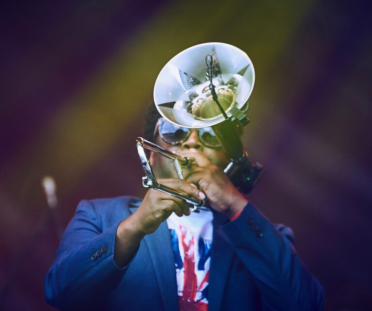 Dennis Rollins wearing a blue blazer and white shirt, playing a trumpet.