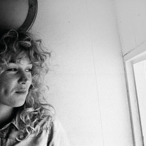 A black and white photography of Beth Rowley looking out a window.