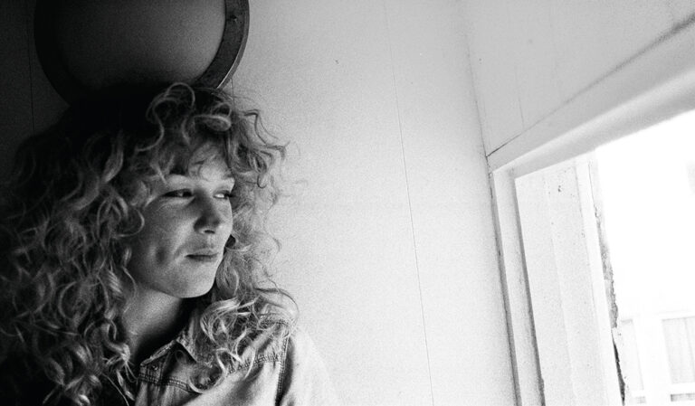 A black and white photography of Beth Rowley looking out a window.