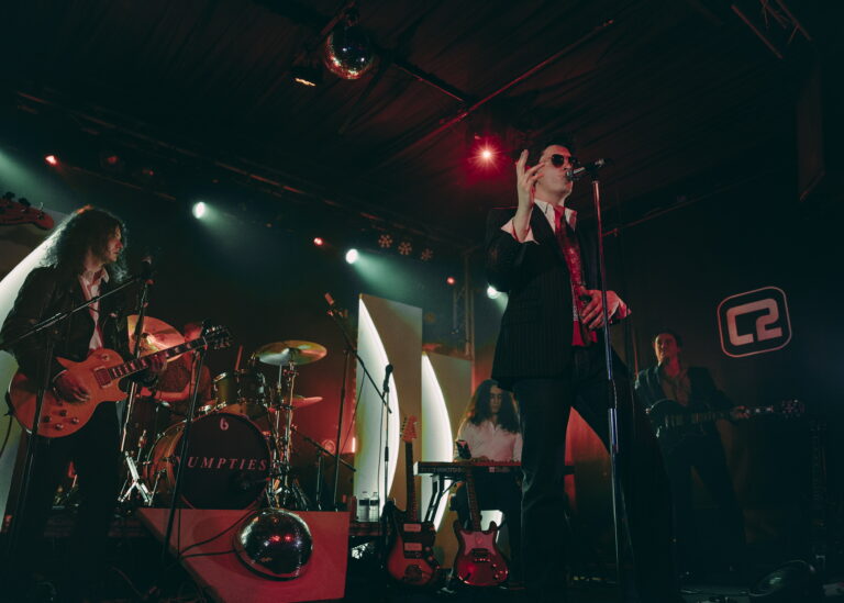 A band of five males on stage - a singer, guitarist, bassist, keyboardist, and drummer.