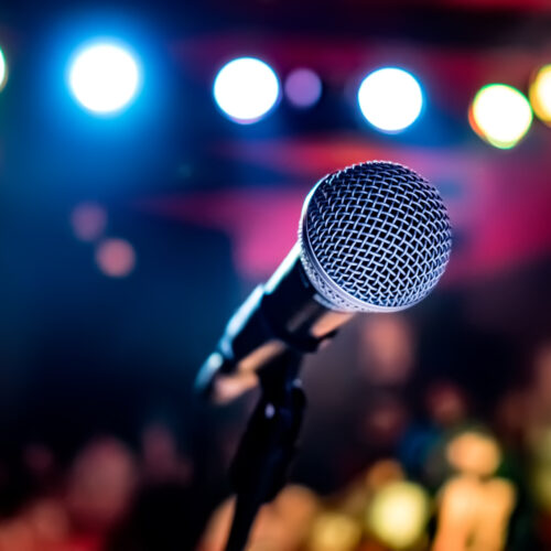 A microphone on a stand in front of a stage with blurred lights.