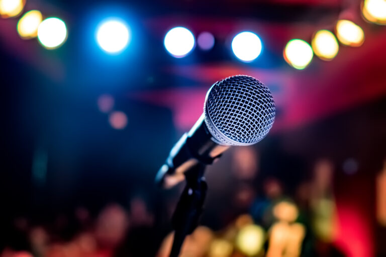 A microphone on a stand in front of a stage with blurred lights.